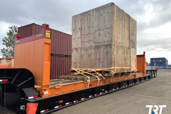 Outdoor storage for oversized cargo — crated load on a flatbed trailer near containers